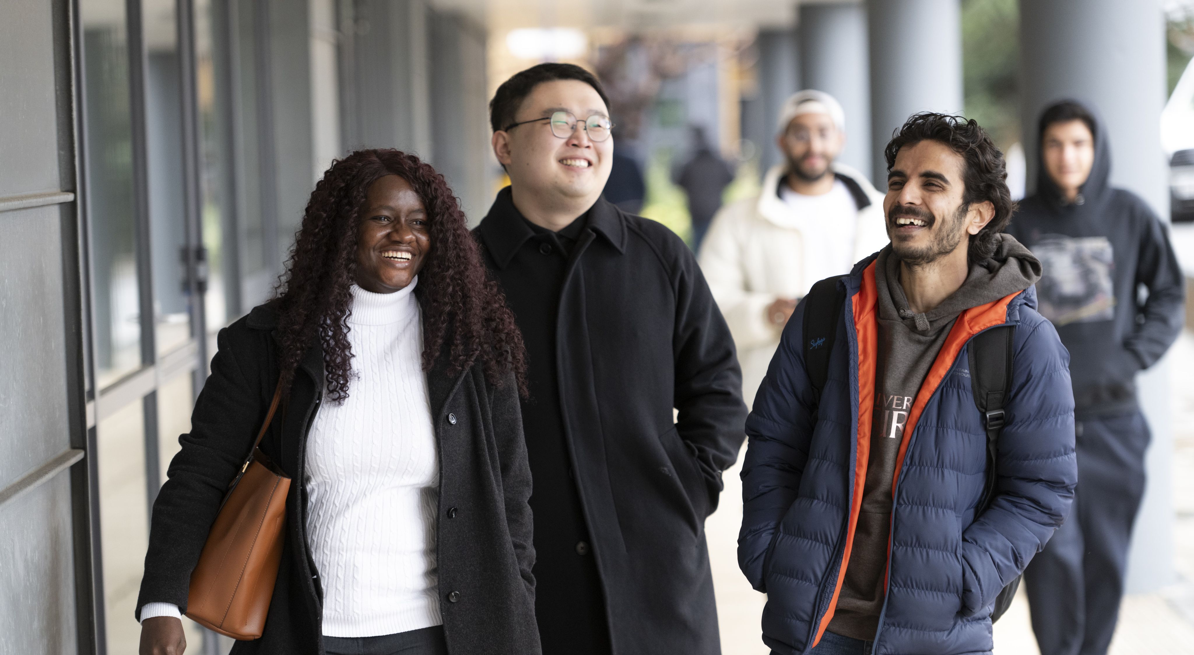 Three students smiling as they walk across Austin Pearce piazza on the University of Surrey's Stag Hill campus