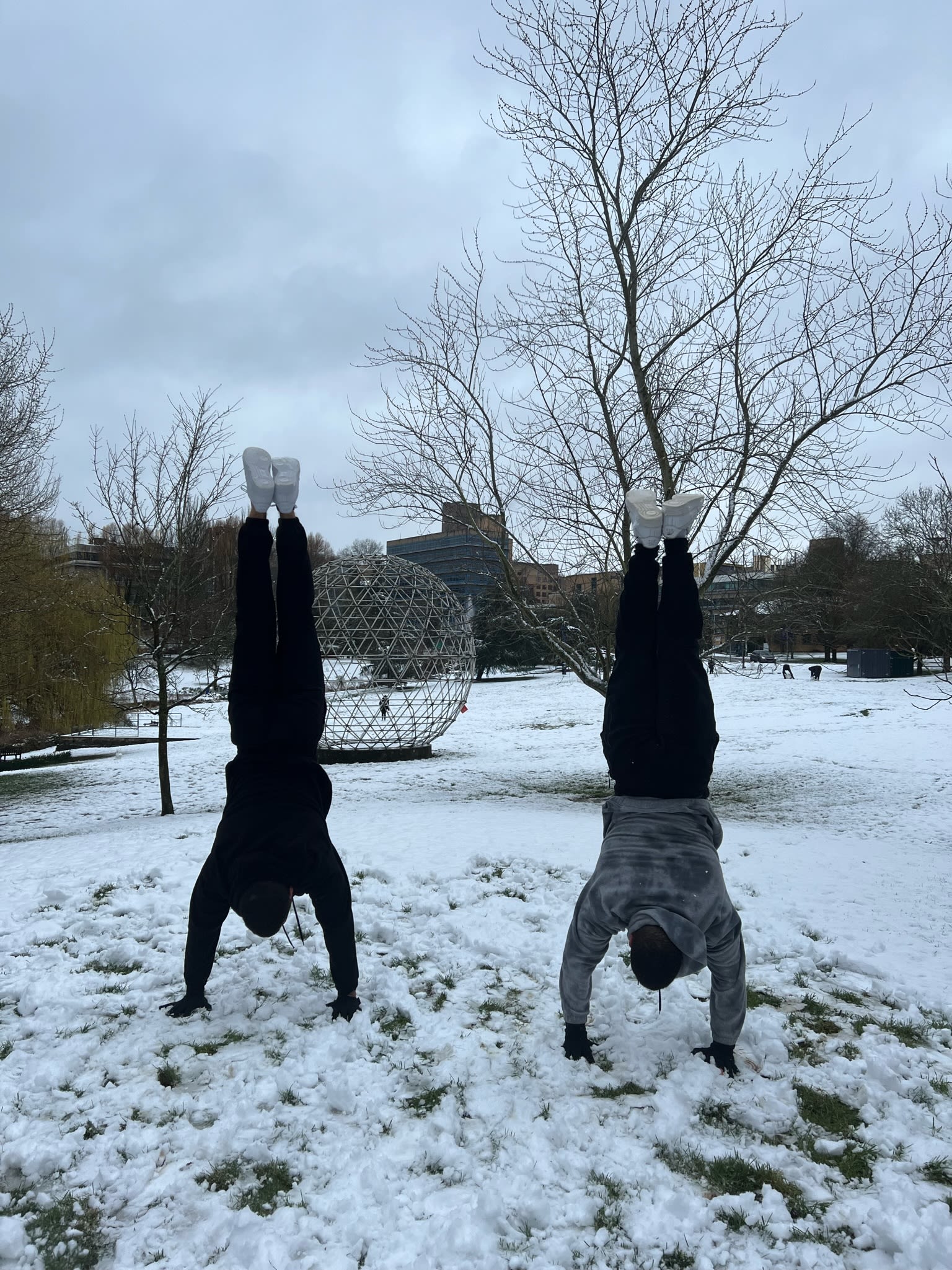 Two people do handstands in the snow by the Lake on Surrey's Stag Hill campus
