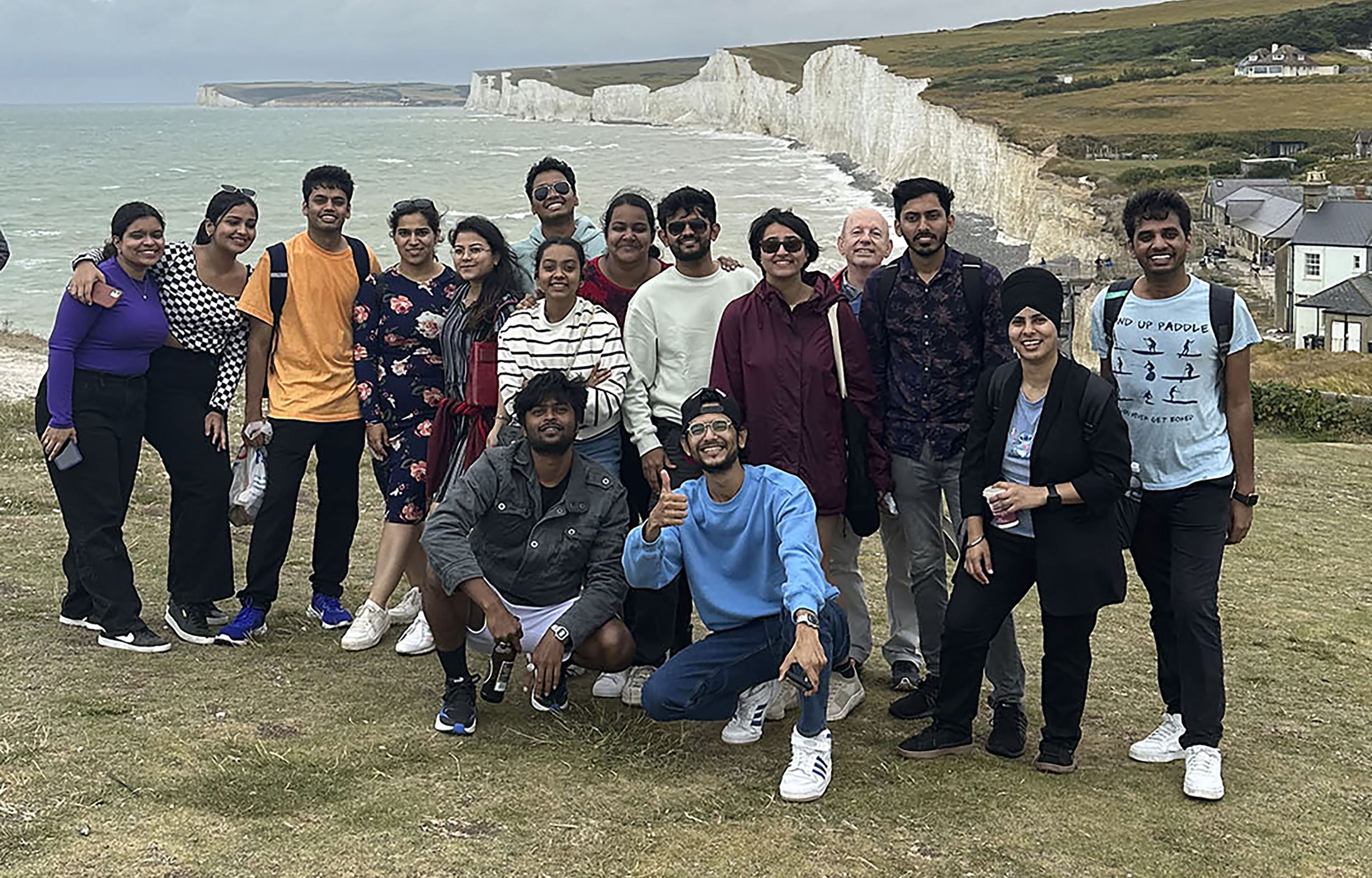 A group - mostly composed of international students - pose for a photo with the chalk cliffs of East Sussex in the background