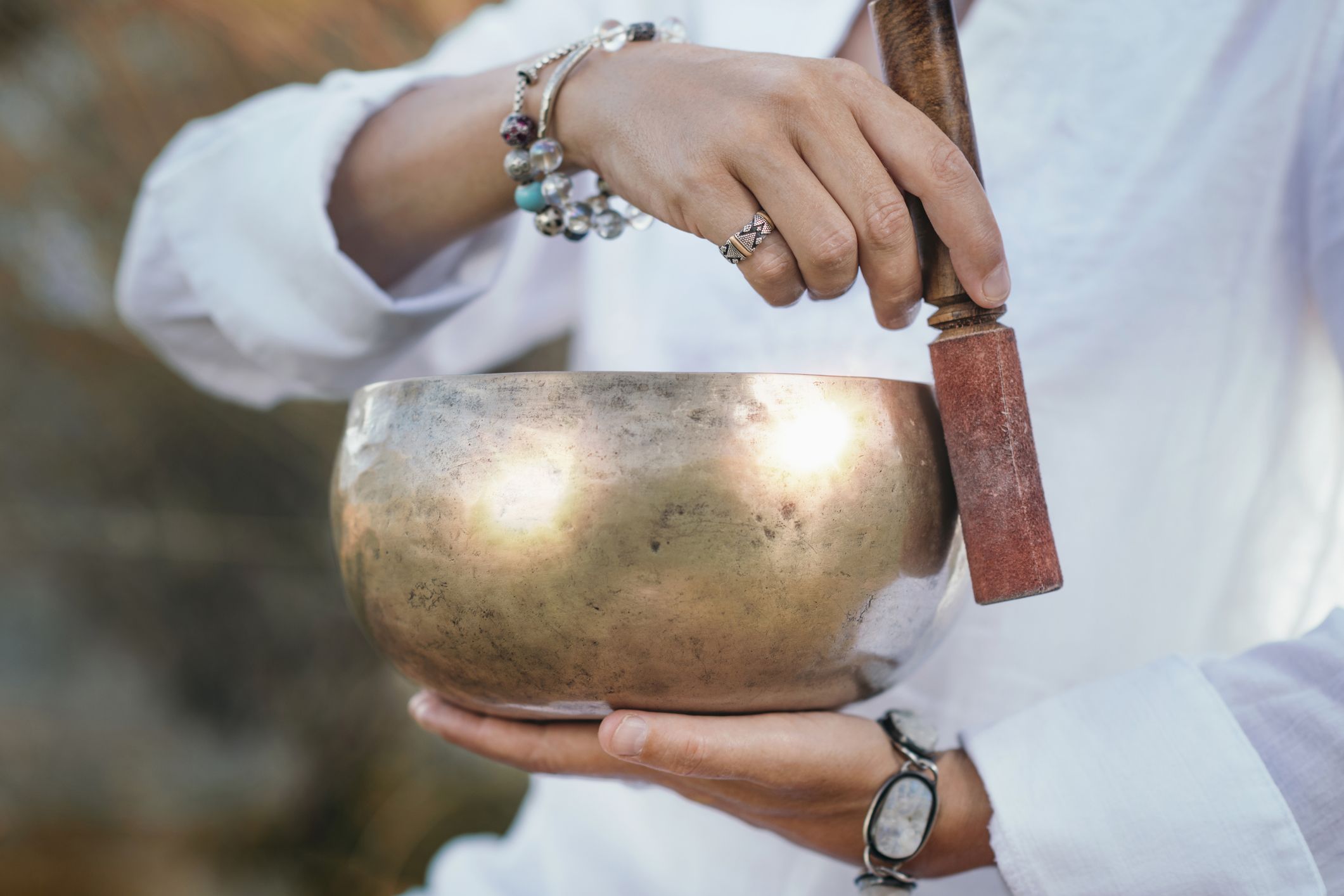 A hand using a wooden tool to create sound with a metal bowl 