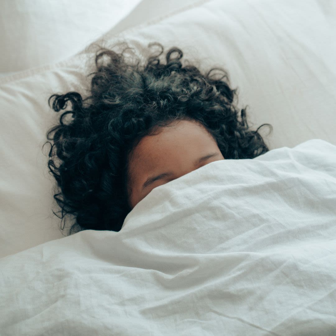 A person with a duvet over their eyes in a bed