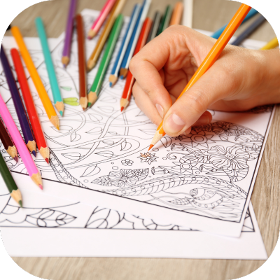 A hand holding an orange pencil colours a flower on a page surrounded by colouring pencils