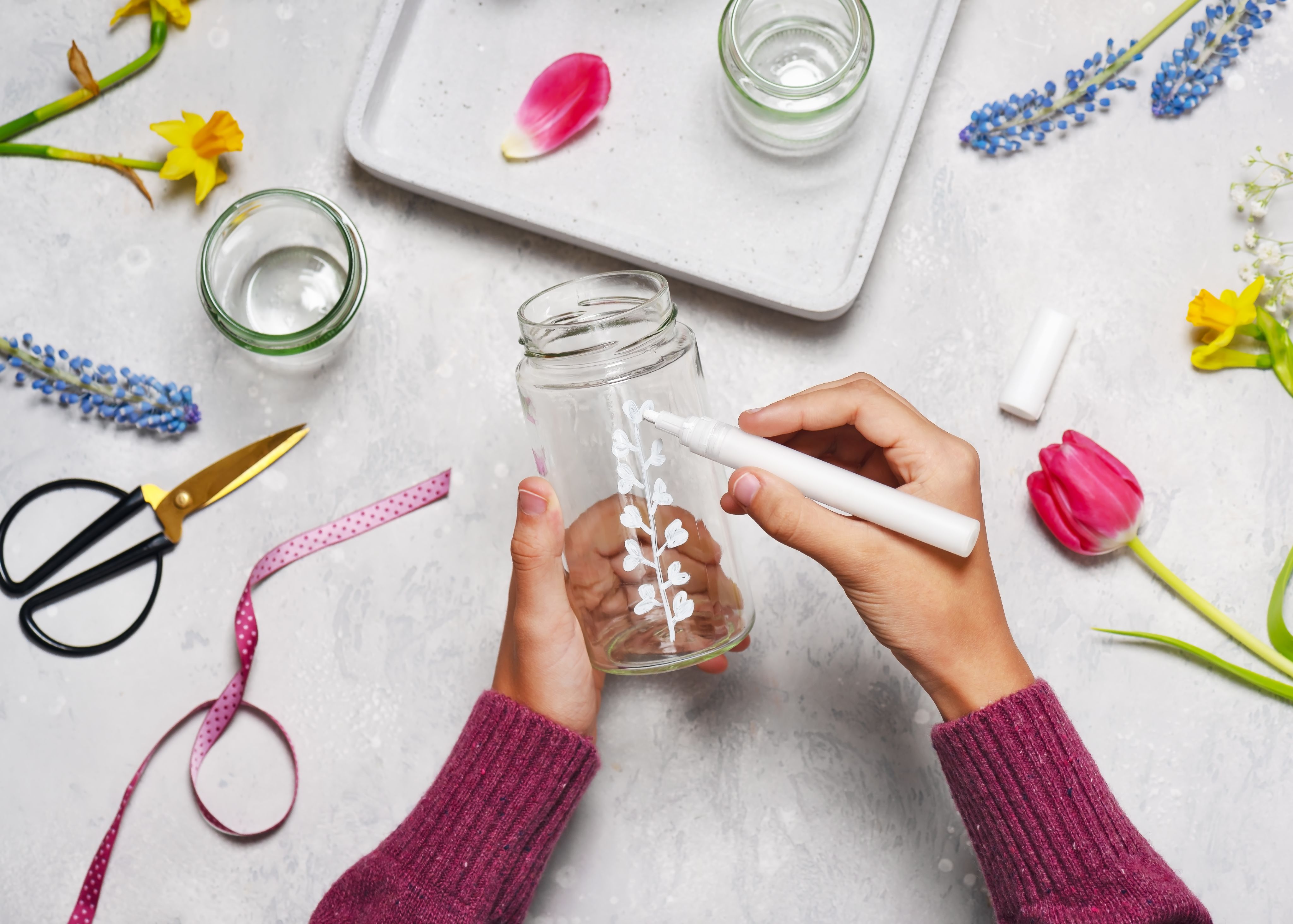 Hands decorating a jar using a white paint pen
