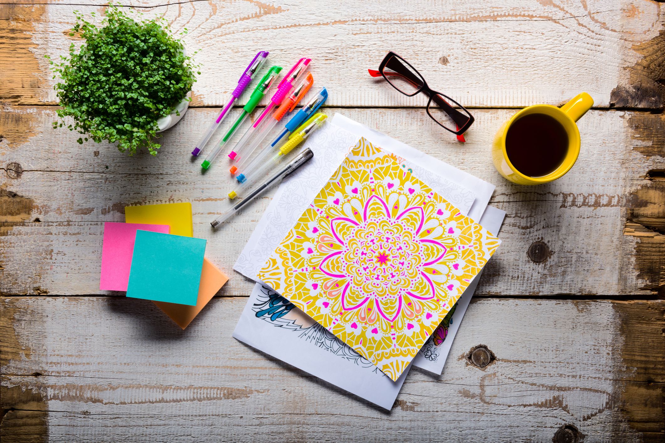 A flatlay of pens, coffee mug, glasses, notebook and post-it notes