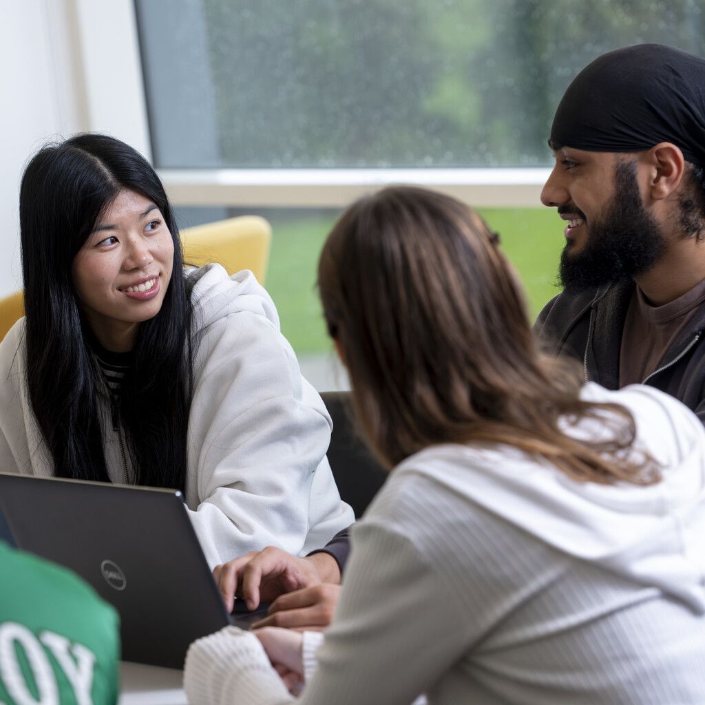 Three students sat with a laptop, smiling