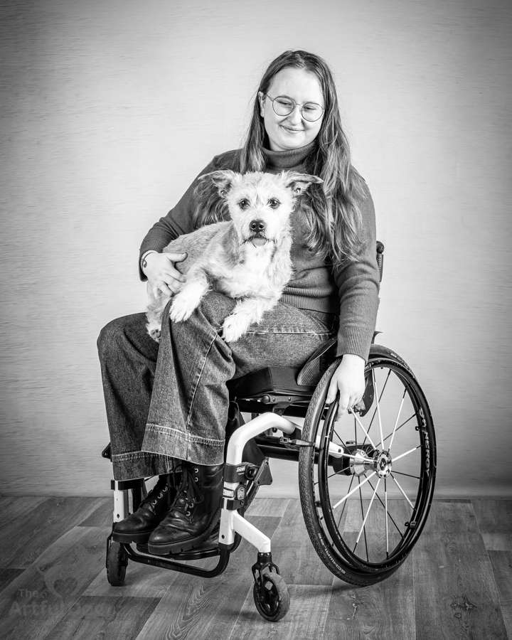A black and white photo of Abi Hayes sat in her wheelchair with a dog on her lap