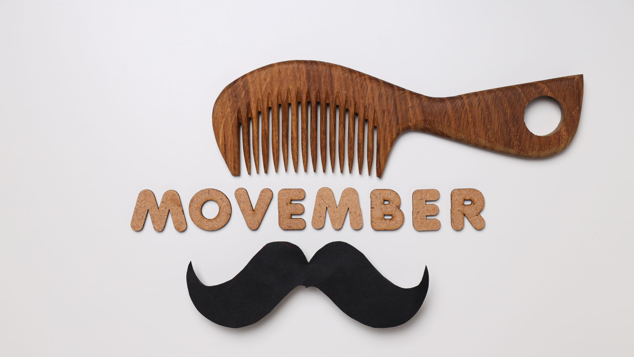 Flatlay of a comb and a cut out moustache with wooden letters spelling out the word Movember
