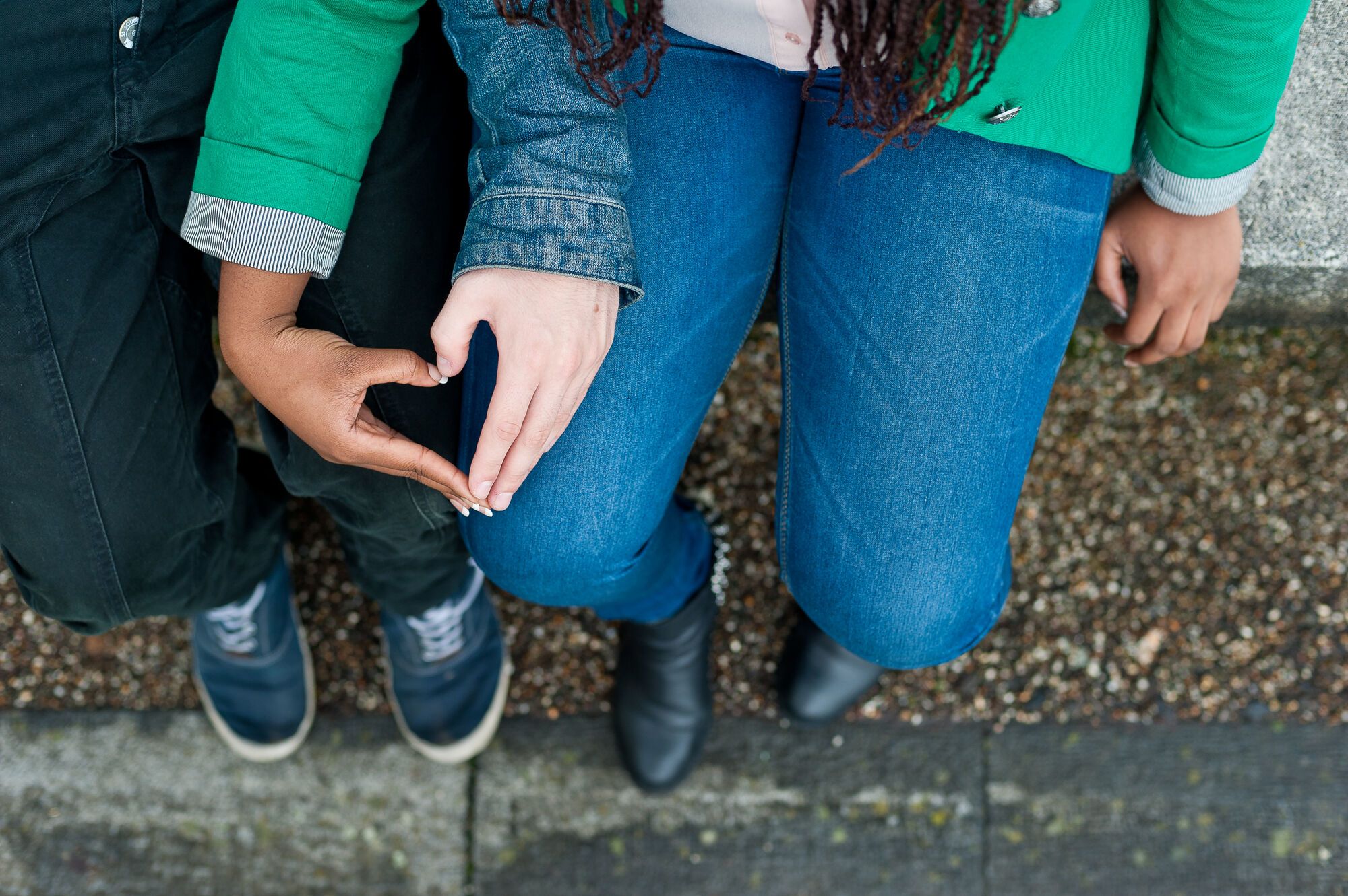 Two people make a heart shape with their hands on their lap