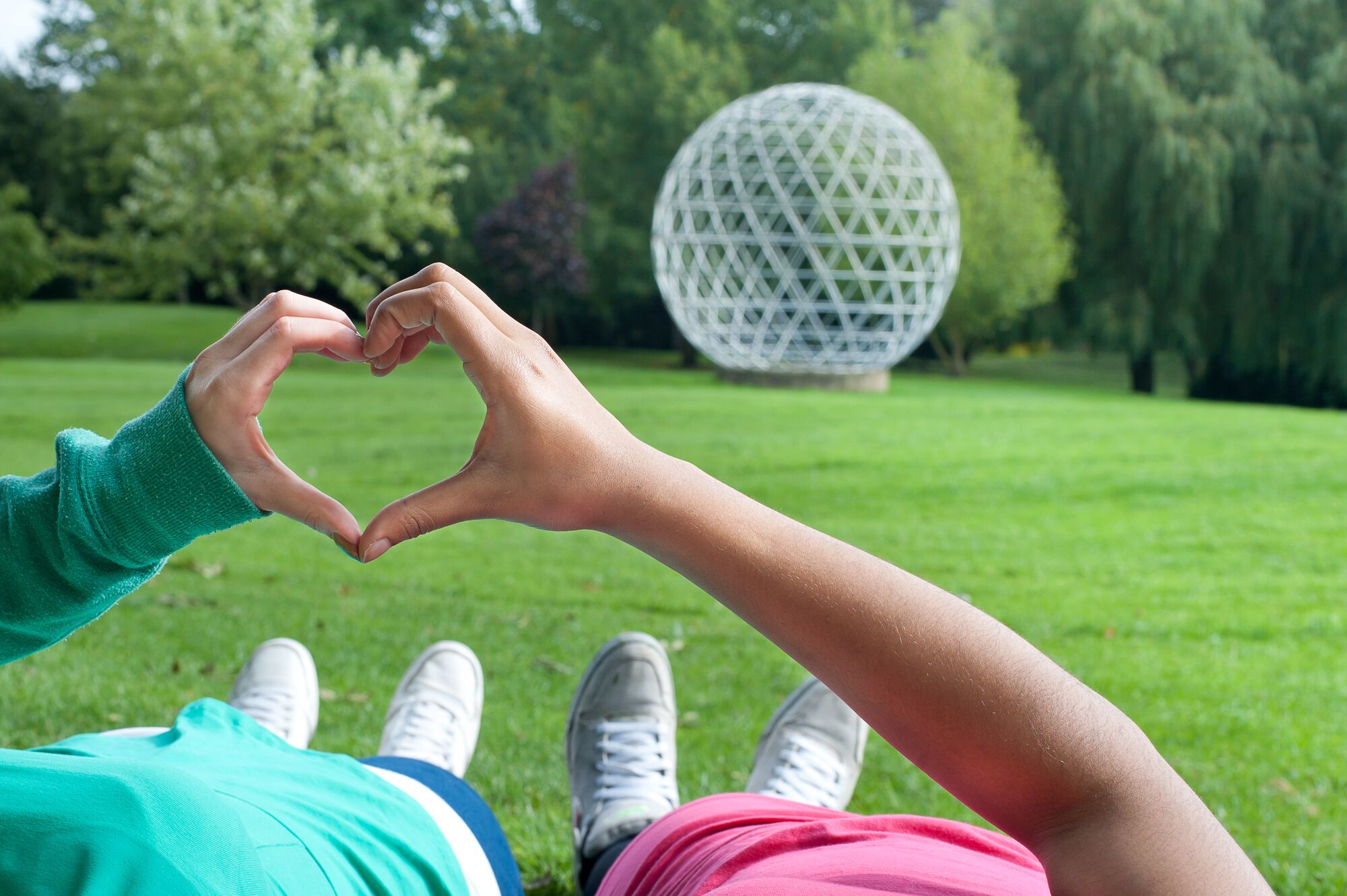 Two people make a heart with their hands with the geodesic dome in the background