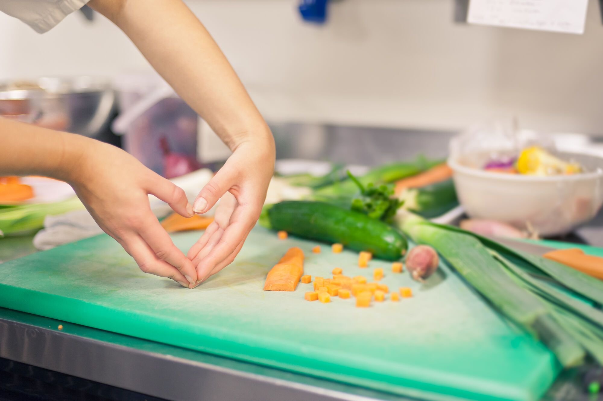 A pair of hands makes a heart shape in front of a chopping board with fresh vegetables being prepared