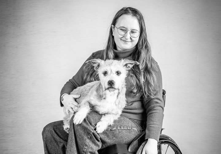 A black and white photo of Abi Hayes sat in her wheelchair with her dog on her lap