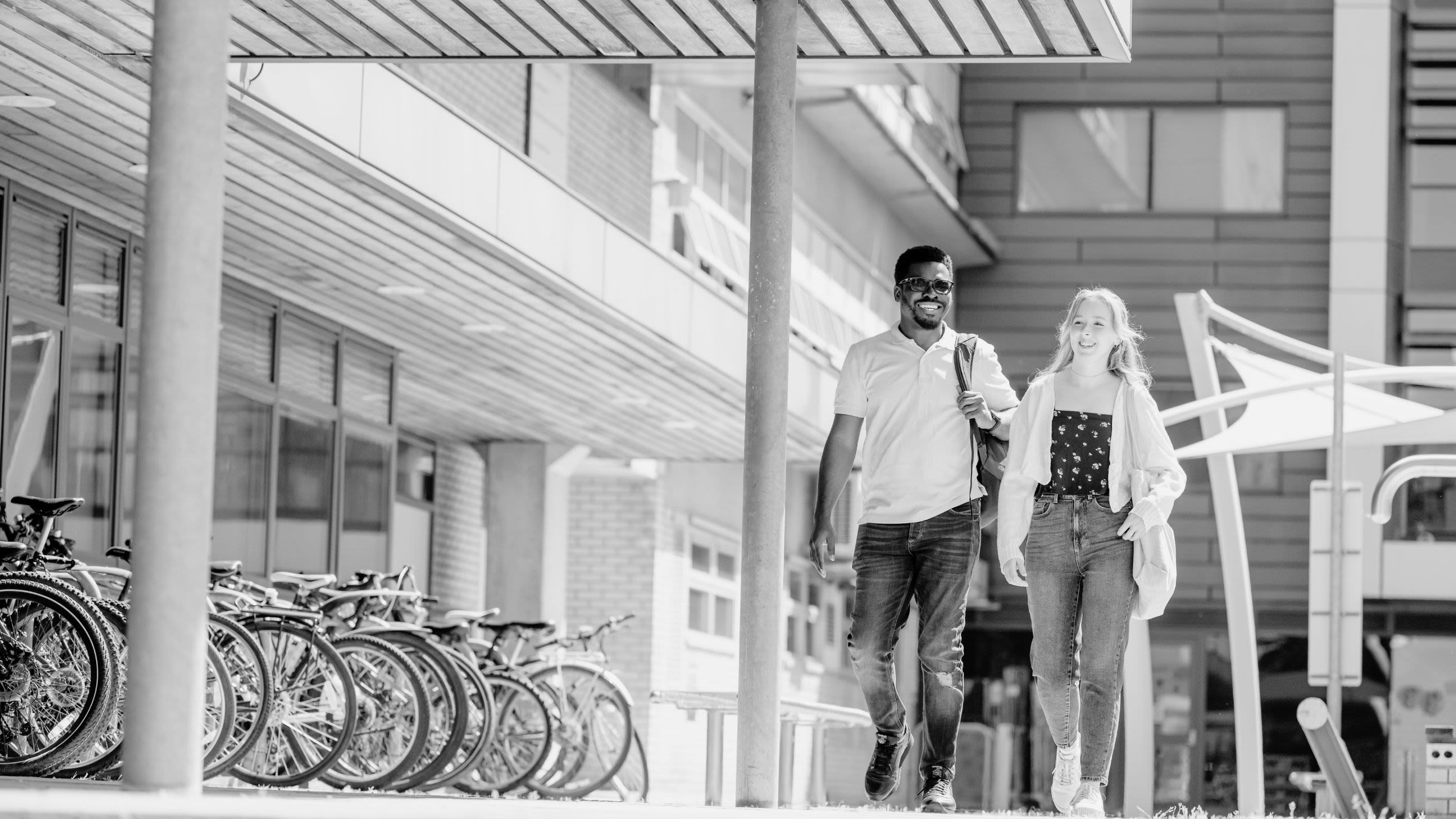 Black and white photo of two students walking past the library on Surrey's Stag Hill campus