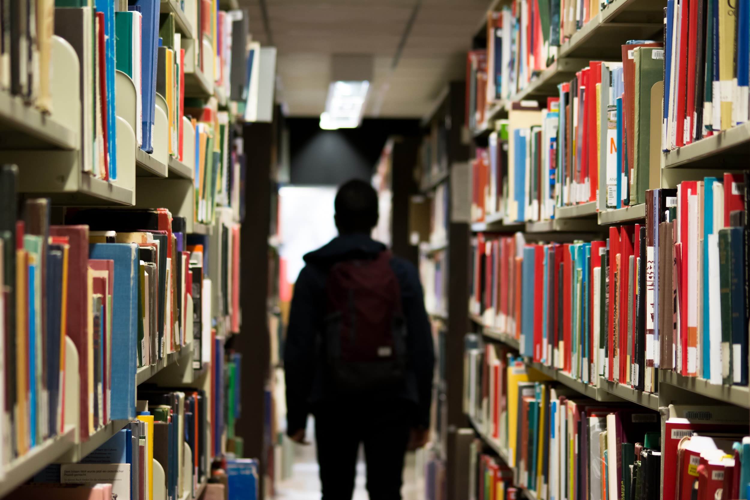 Photo by Redd F on Unsplash - man with backpack beside a books