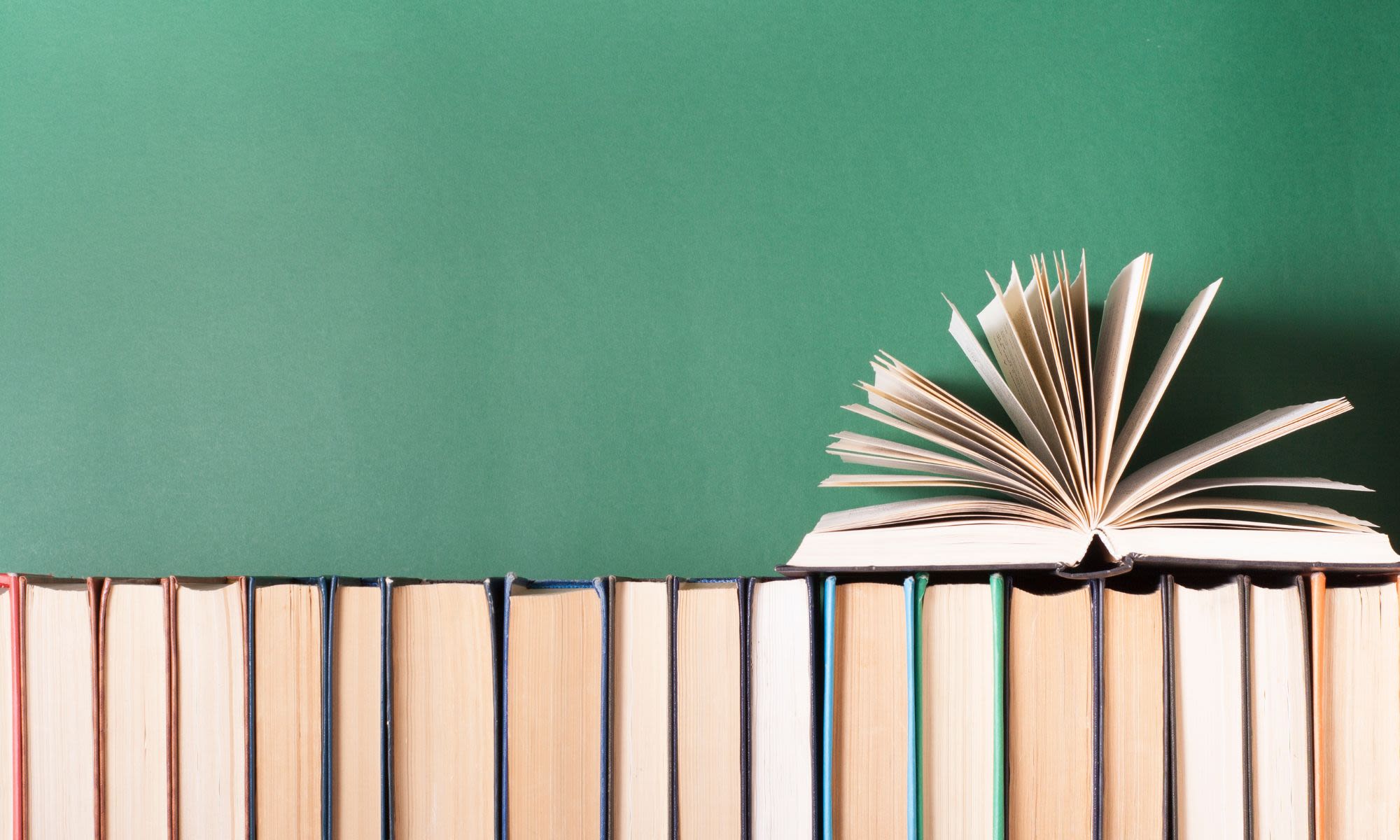 Hardback books lined up against a green wall