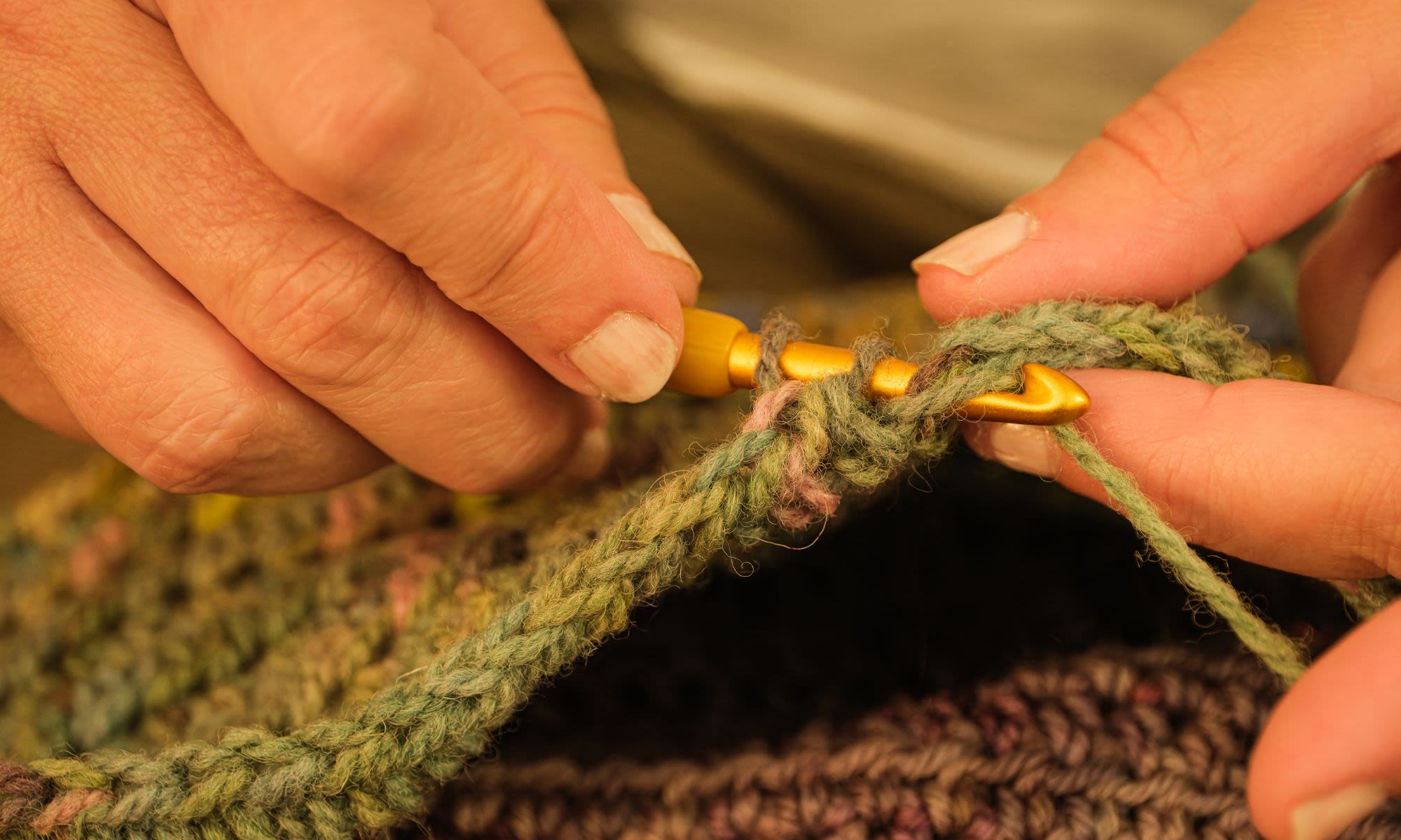 A pair of hands use a crochet hook to create a green item