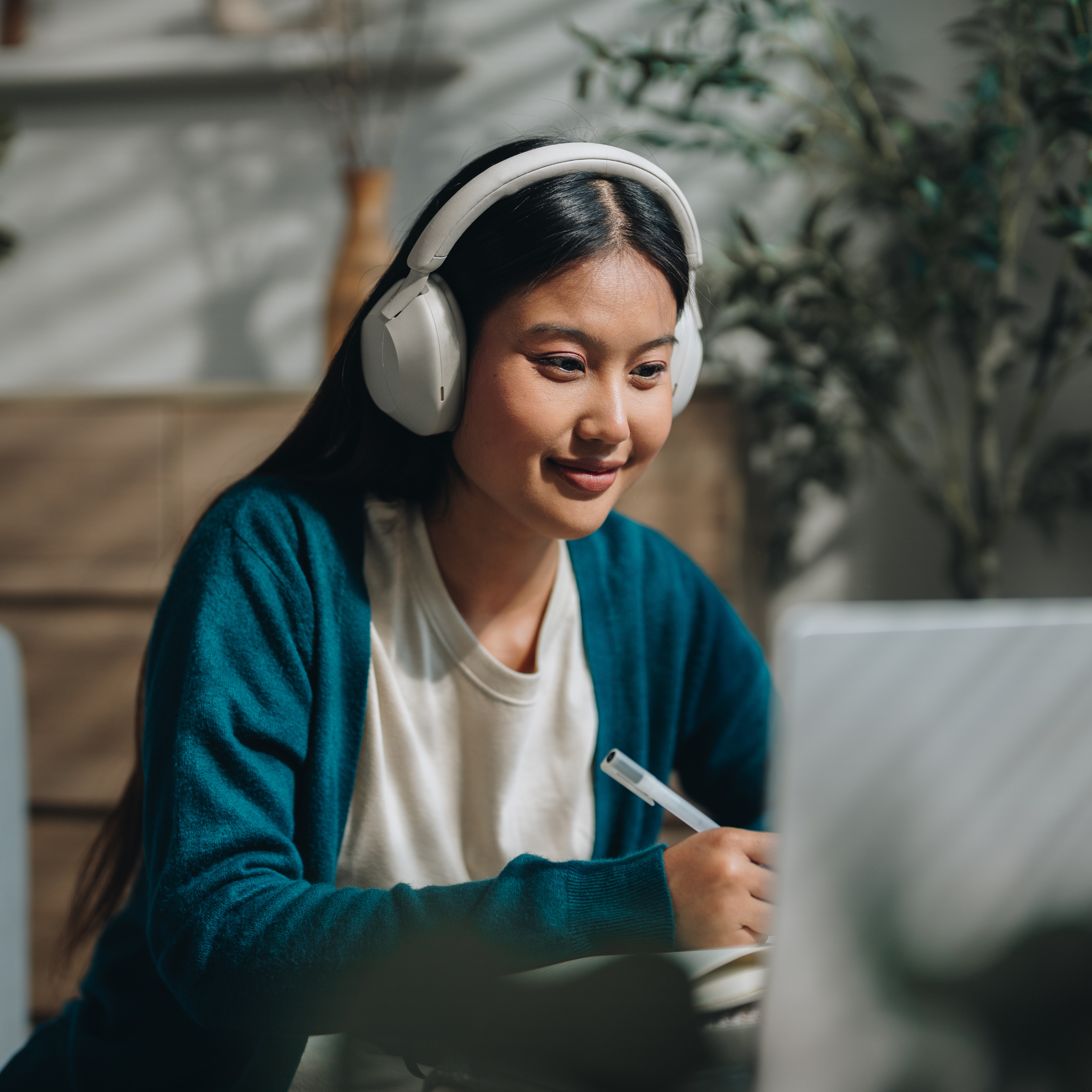Student with headphones in, watching her laptop and writing