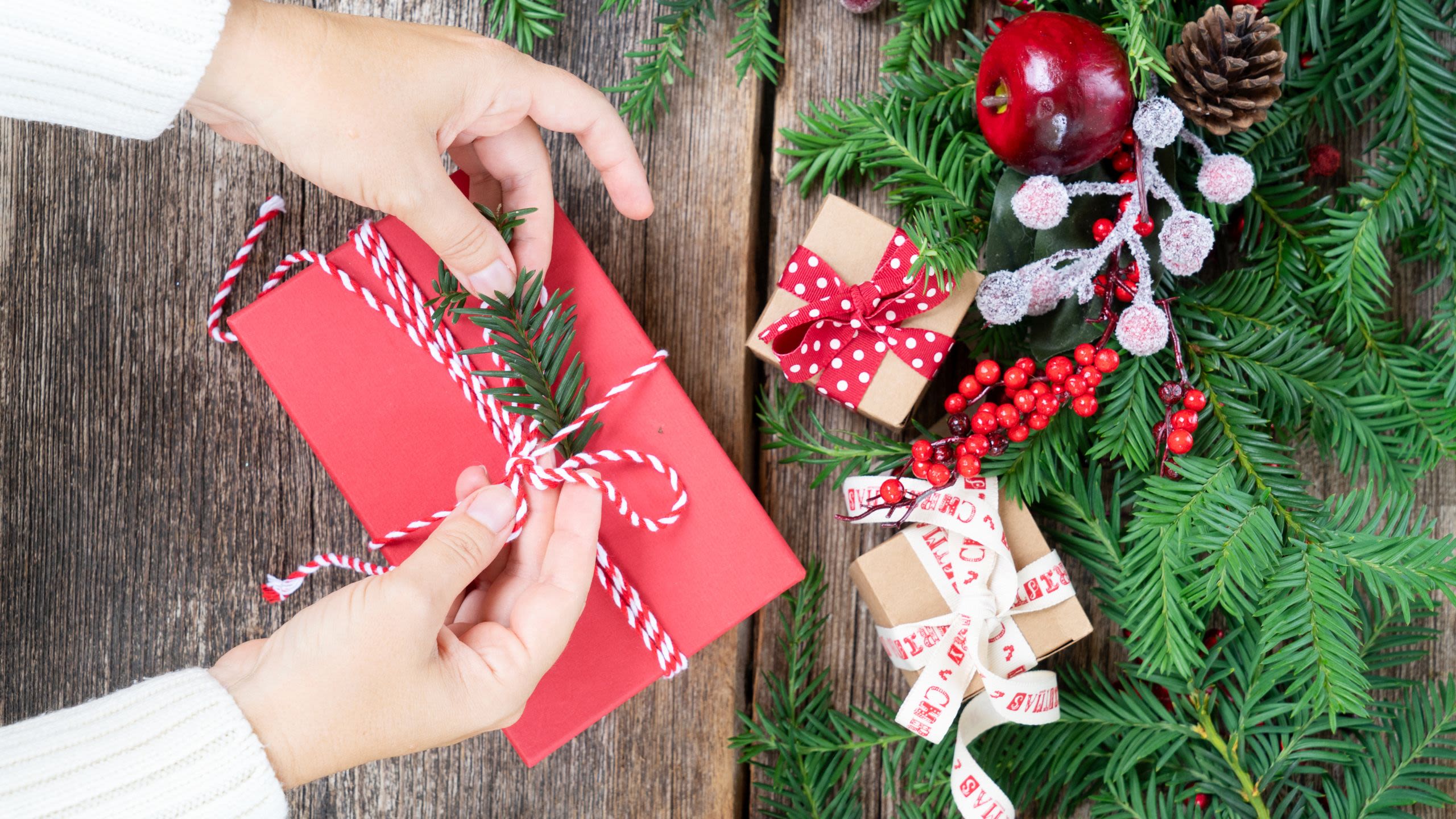 A pair of hands tie a Christmas gift wrapped with sustainable materials