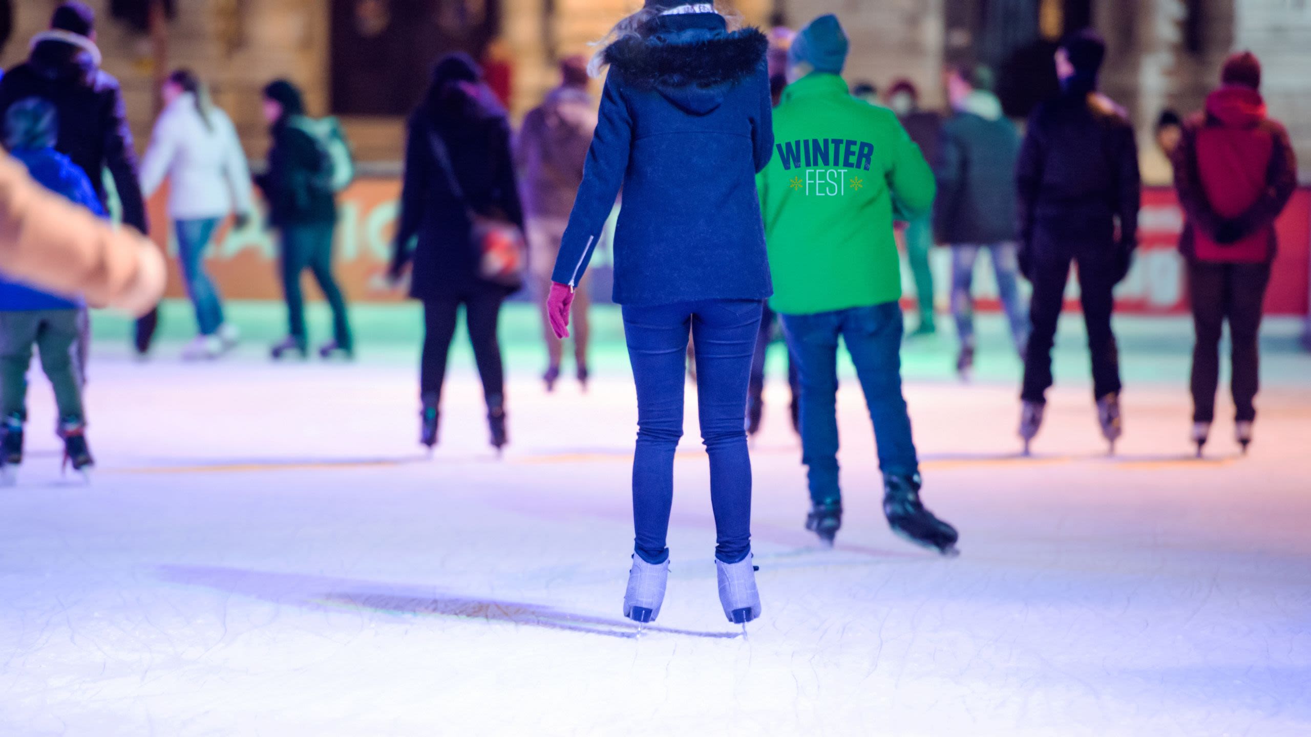 People wrapped in warm clothing skate around an ice rink