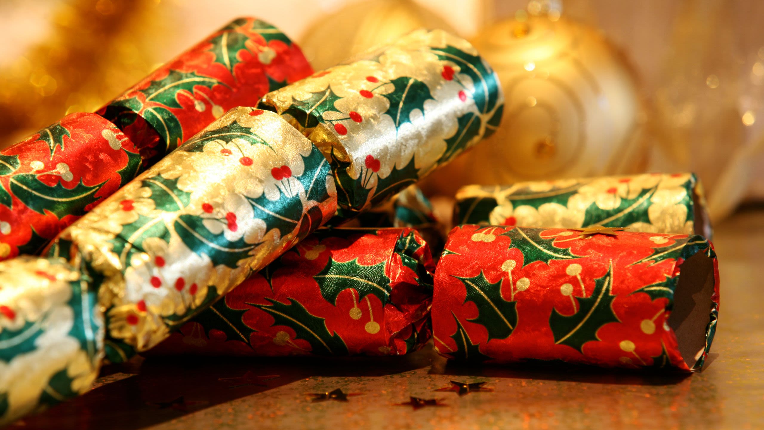 Two red and two gold Christmas crackers with holly markings lie on a table