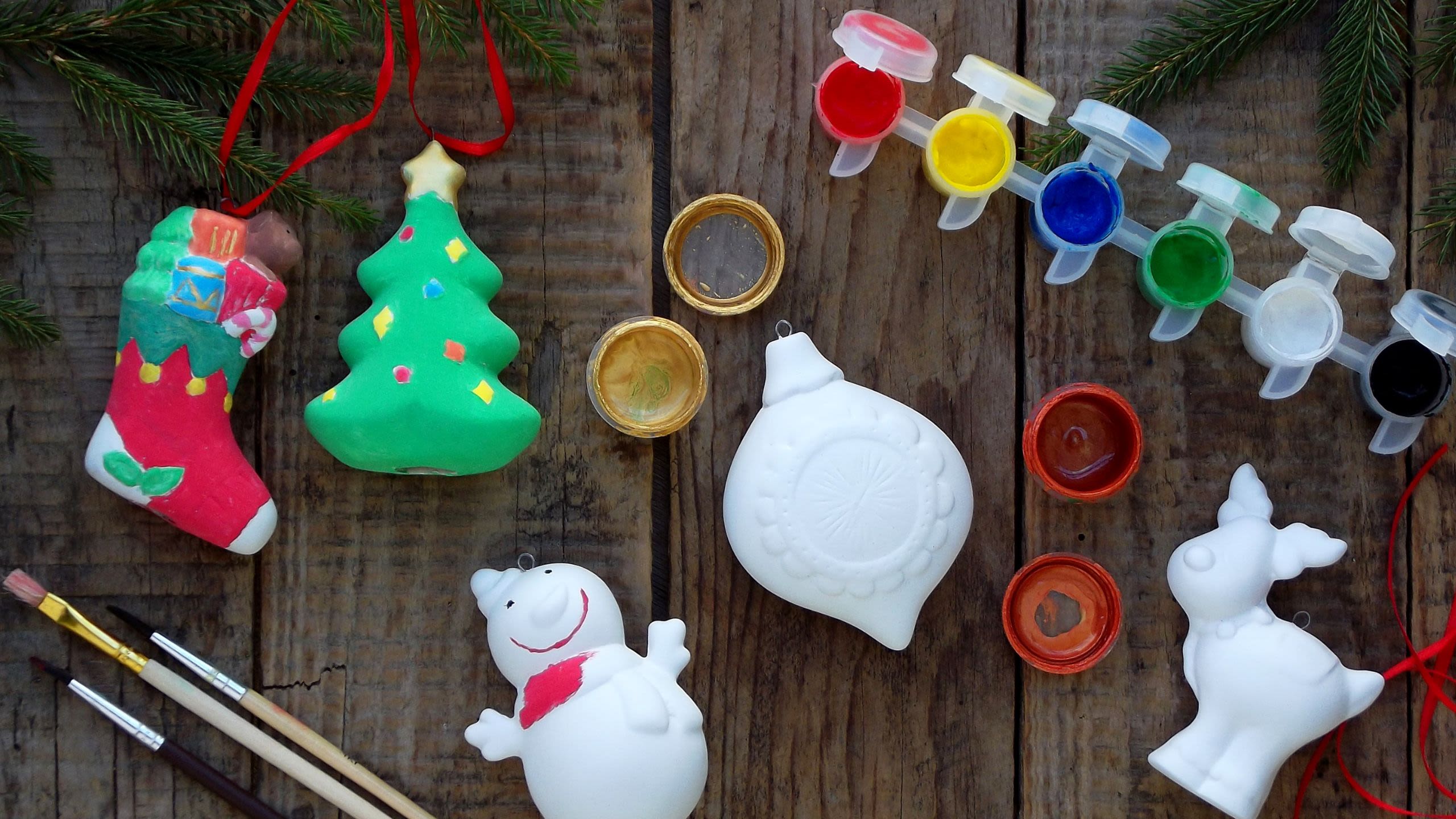 Flat lay of ceramic ornaments (snowman, reindeer, christmas tree, bauble and stocking), paint and paintbrushes